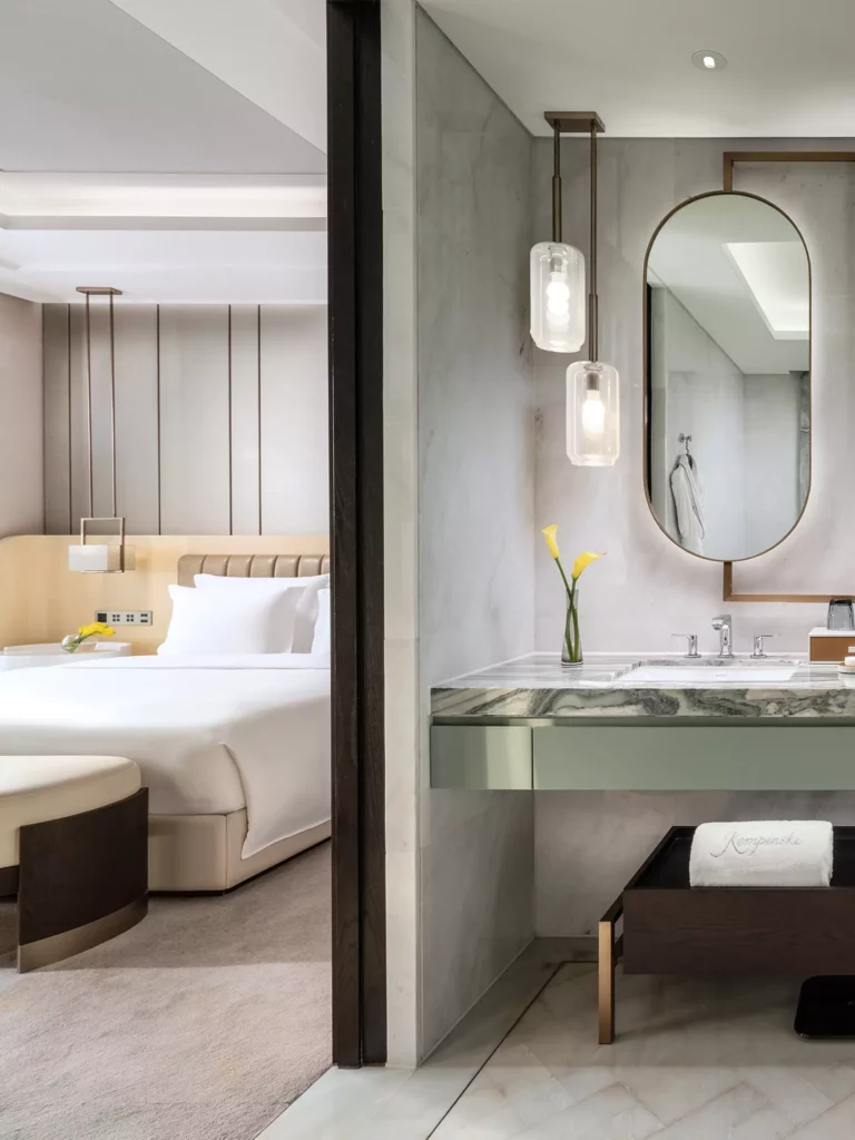 Luxuriöses Hotelzimmer mit großem Bett, modernem Badezimmer mit Marmorwaschtisch, ovalem Spiegel und gelben Blumen im